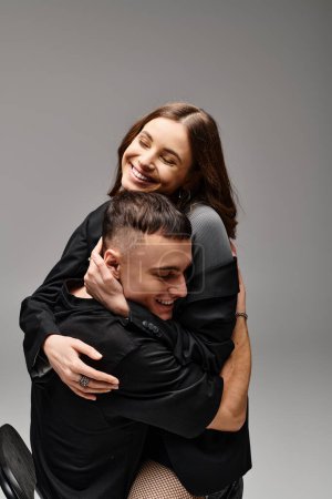 Ein Mann und eine Frau umarmen sich innig und drücken in einem Studio vor grauem Hintergrund Zuneigung und Nähe aus.