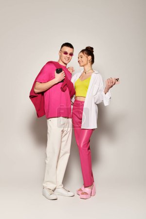 A stylish young couple stands close together, exuding love and connection in a studio against a grey background.