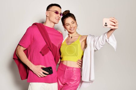 Téléchargez les photos : Un jeune couple élégant amoureux prenant un selfie ensemble dans un studio avec un fond gris. - en image libre de droit