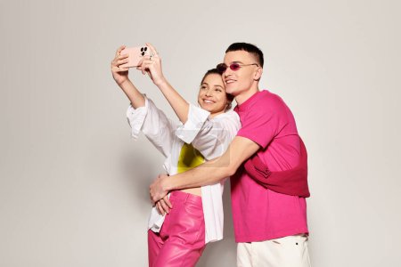 Una elegante pareja joven enamorada se toma una selfie juntos en un estudio con un fondo gris.