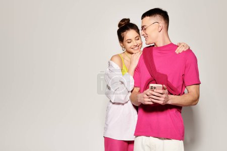 A stylish young man and woman standing close together in a studio, expressing love and connection against a grey background.