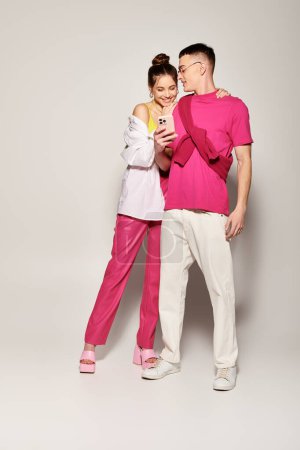A stylish young man and woman stand next to each other, expressing love and connection in a studio with a grey background.