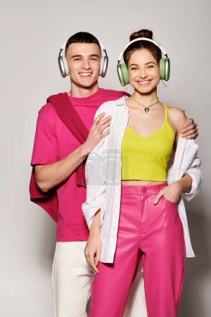 Ein stylisches junges Paar, tief verliebt, hört gemeinsam Musik und trägt Kopfhörer vor einem glatten grauen Hintergrund..