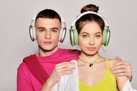 Ein stilvolles junges verliebtes Paar mit Kopfhörern, eingetaucht in die Musik vor grauem Studiohintergrund.