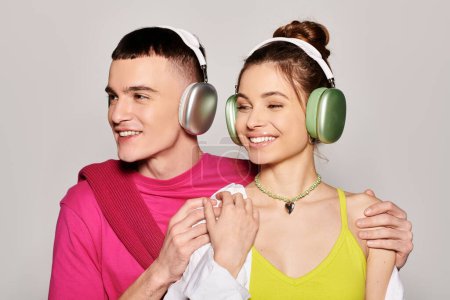 Téléchargez les photos : Un jeune couple élégant amoureux, écoutant de la musique avec un casque dans un studio avec un fond gris. - en image libre de droit