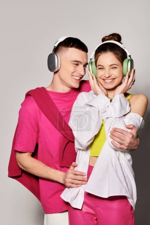 Foto de Una elegante pareja joven enamorada escuchando música juntos, usando auriculares contra un fondo gris de estudio. - Imagen libre de derechos