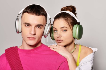 Photo for A stylish young couple, deeply in love, wearing headphones and enjoying music together in a studio with a grey background. - Royalty Free Image