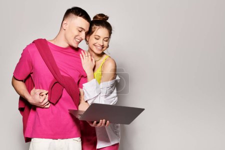 Téléchargez les photos : Un jeune couple élégant se tient avec ordinateur portable côte à côte dans un studio avec un fond gris. - en image libre de droit