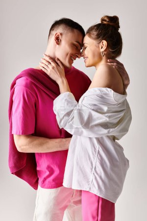 Foto de Un hombre y una mujer, vestidos con estilo, se paran uno al lado del otro en un estudio sobre un fondo gris, mirándose cariñosamente. - Imagen libre de derechos