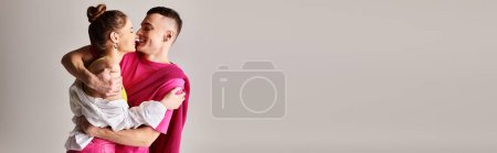 Téléchargez les photos : Un jeune homme élégant tient tendrement son partenaire dans ses bras sur fond de studio gris. - en image libre de droit