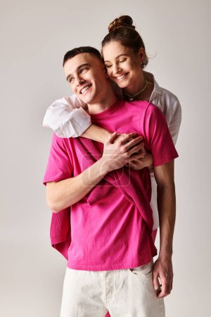 Photo for A man affectionately hugs a woman wearing a pink shirt in a stylish studio setting with a grey background. - Royalty Free Image