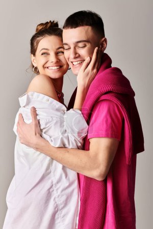 Un jeune couple élégant amoureux, se serrant dans ses bras avec une véritable affection, debout sur un fond de studio gris.