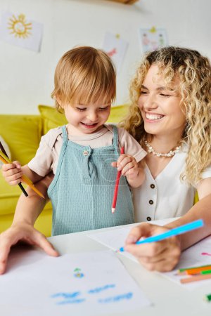 Lockige Mutter und Kleinkind-Tochter erkunden Montessori-Methode und beschäftigen sich freudig mit Buntstiften.