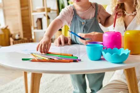 A curly mother and her toddler daughter are deeply engrossed in Montessori learning activities at a table.