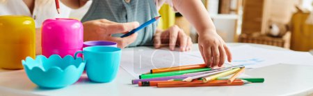 Una mujer se sienta en una mesa, enfocada en un montón de crayones con su hija pequeña, abrazando el método Montessori de educación.
