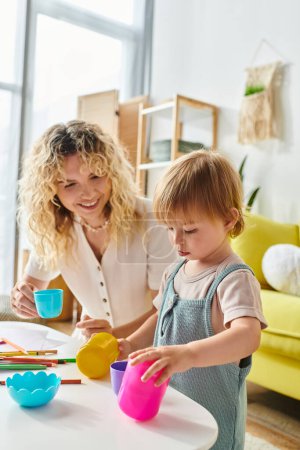Photo for A curly mother and her toddler daughter engage in playful Montessori cup activities at home. - Royalty Free Image