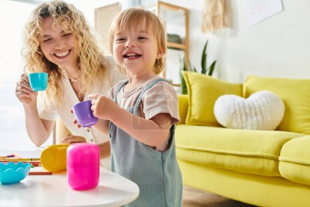 Curly mother and her toddler daughter playfully explore Montessori cup activities at home.