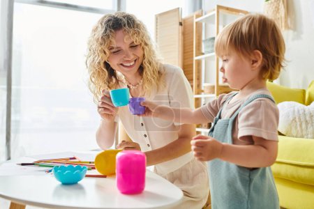 A woman with curly hair interacts with her toddler daughter at a table, engaging in Montessori method activities.