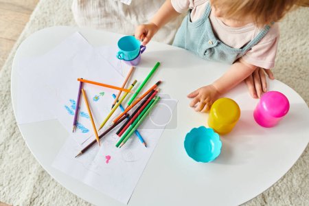 A little girl is happily playing with colored crayons on a table as part of a Montessori educational activity at home.