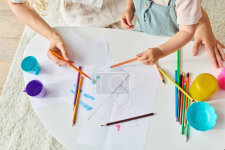 tout-petit et maman s'assoient à une table de dessin avec des crayons de couleur et des crayons.