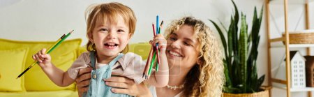 Photo for Curly mother and her toddler daughter holding crayons, using Montessori method. - Royalty Free Image