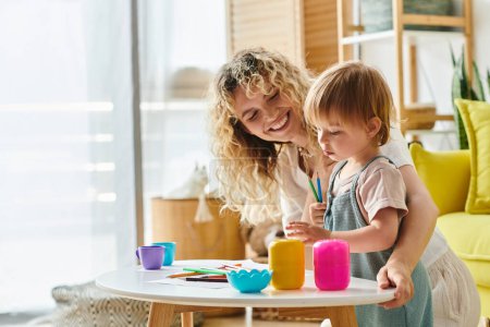Eine lockige Mutter und ihre kleine Tochter erforschen und lernen spielerisch, während sie Tassen in einer Montessori-inspirierten Aktivität zu Hause verwenden.
