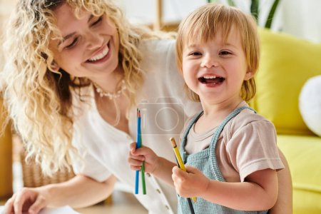 Photo for A curly-haired mother and her toddler daughter hold pencils in their hands, engaging in the Montessori method of education at home. - Royalty Free Image