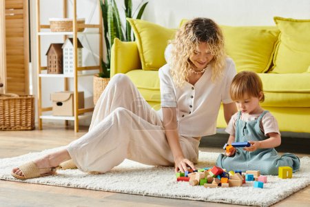 Eine Frau mit lockigem Haar spielt mit ihrer Kleinkind-Tochter auf dem Fußboden und übt sich in Montessori-Erziehung und -Bindung.