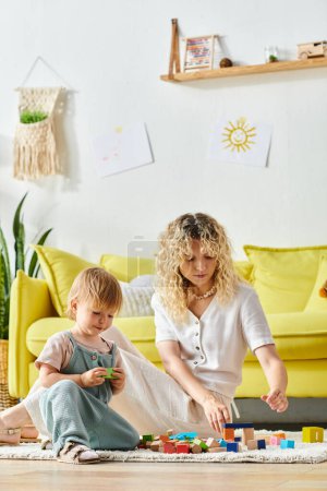 Lockenmähnige Mutter legt sich freudig mit ihrer Kleinkind-Tochter auf den Boden und benutzt dabei die Montessori-Erziehungsmethode.