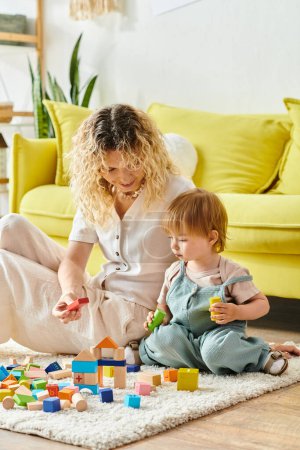 Photo for A curly mother is joyfully playing with her toddler daughter on the floor at home, using the Montessori method of education. - Royalty Free Image