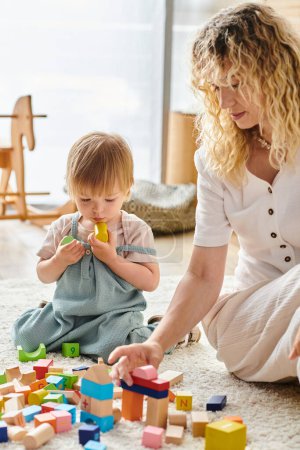 Téléchargez les photos : A curly mother and her toddler daughter interact playfully on the floor using the Montessori method of education. - en image libre de droit