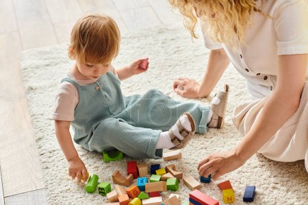 Téléchargez les photos : Une mère frisée s'engage joyeusement avec sa fille tout-petit sur le sol, en utilisant l'éducation Montessori à la maison. - en image libre de droit
