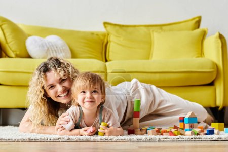 Foto de A curly mother and her toddler daughter engage in Montessori learning, sprawled comfortably on the floor at home. - Imagen libre de derechos