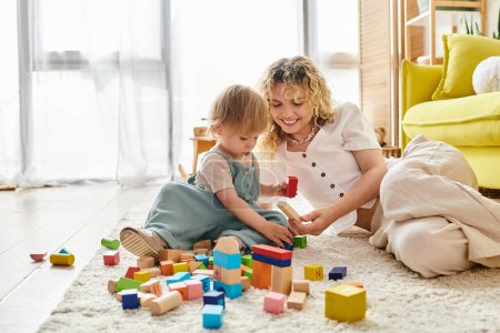 A curly mother and toddler daughter enjoy a playful moment on the floor, building structures with colorful blocks.