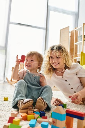 A curly-haired mother and her toddler daughter engage in educational play with blocks on the floor.