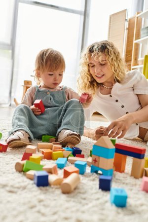 A curly mother and her toddler daughter bonding and learning through play with blocks on the floor at home.