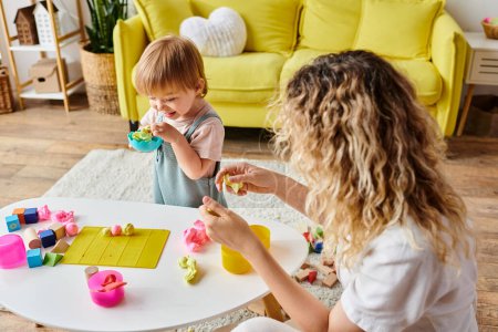 Foto de Una mujer con el pelo rizado y su hija pequeña profundamente comprometida en Montessori jugar con juguetes de colores en casa. - Imagen libre de derechos