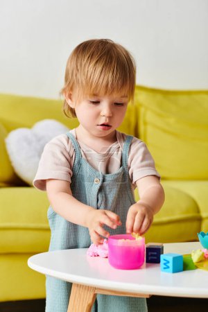 Téléchargez les photos : Une petite fille engloutie dans le jeu avec un jouet sur une table à la maison, explorer, apprendre et s'amuser. - en image libre de droit
