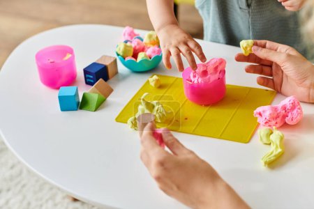 Téléchargez les photos : Un enfant est engagé dans le moulage de pâte à jouer colorée sur une table, explorant la créativité avec la méthode Montessori. - en image libre de droit