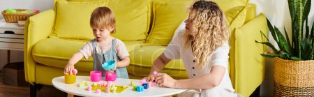 Lockige Mutter und ihre kleine Tochter üben Montessori-Unterricht aus, indem sie mit Klötzen auf einem Tisch spielen.