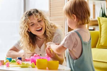 Eine Frau mit lockigem Haar interagiert mit ihrer Kleinkind-Tochter nach Montessori-Methoden an einem Tisch.
