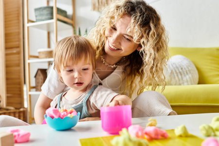 A curly-haired mother and her toddler daughter sit at a table, engrossed in Montessori learning activities at home.