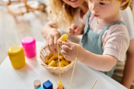 A curly-haired mother and her toddler daughter are playfully exploring different foods together, embracing the Montessori method at home.
