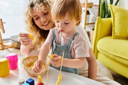 Une mère aux cheveux bouclés et sa fille tout-petit apprennent de manière créative avec des pâtes sèches en utilisant la méthode Montessori à la maison.