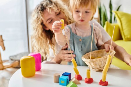 Foto de Una madre rizada y su hija pequeña juguetoneando con juguetes Montessori, fomentando el aprendizaje práctico y la creatividad. - Imagen libre de derechos