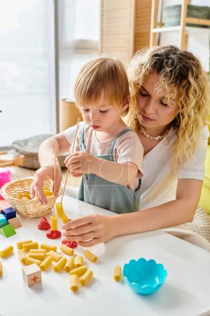 A curly mother and her toddler daughter engage in playful food exploration, embracing Montessori education at home.