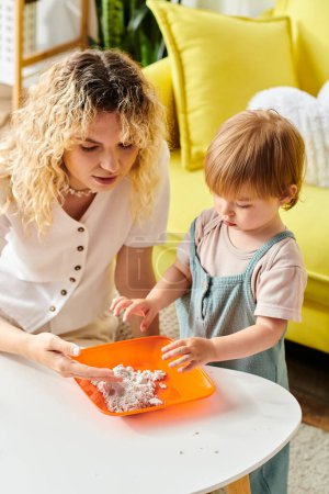 Eine lockige Mutter und ihre kleine Tochter bei Montessori-Aktivitäten mit einem orangefarbenen Tablett zu Hause.