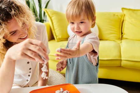 A curly mother and her toddler daughter playfully explore and experiment with various food items using the Montessori education method at home.