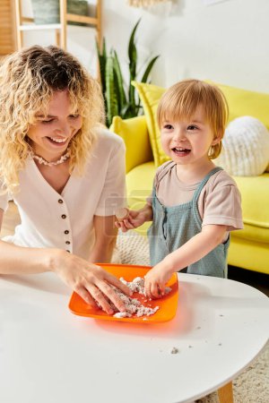 Lockige Mutter und kleine Tochter lernen spielerisch mit einer orangefarbenen Schale und umarmen die Montessori-Methode zu Hause.