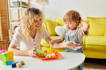 Photo for A curly-haired mother actively engages with her toddler daughter using Montessori method at a table. - Royalty Free Image